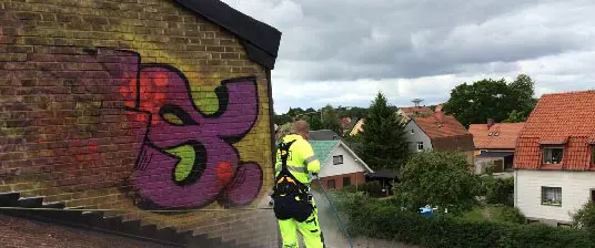 Person som tar bort klotter från en vägg med hjälp av en högtryckstvätt.