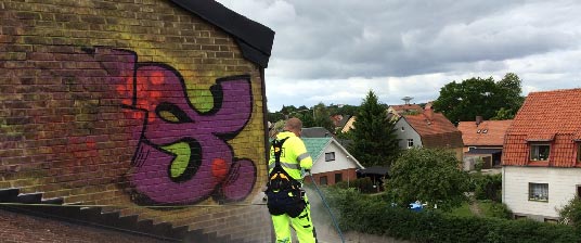 Person som tar bort klotter från en vägg med hjälp av en högtryckstvätt.